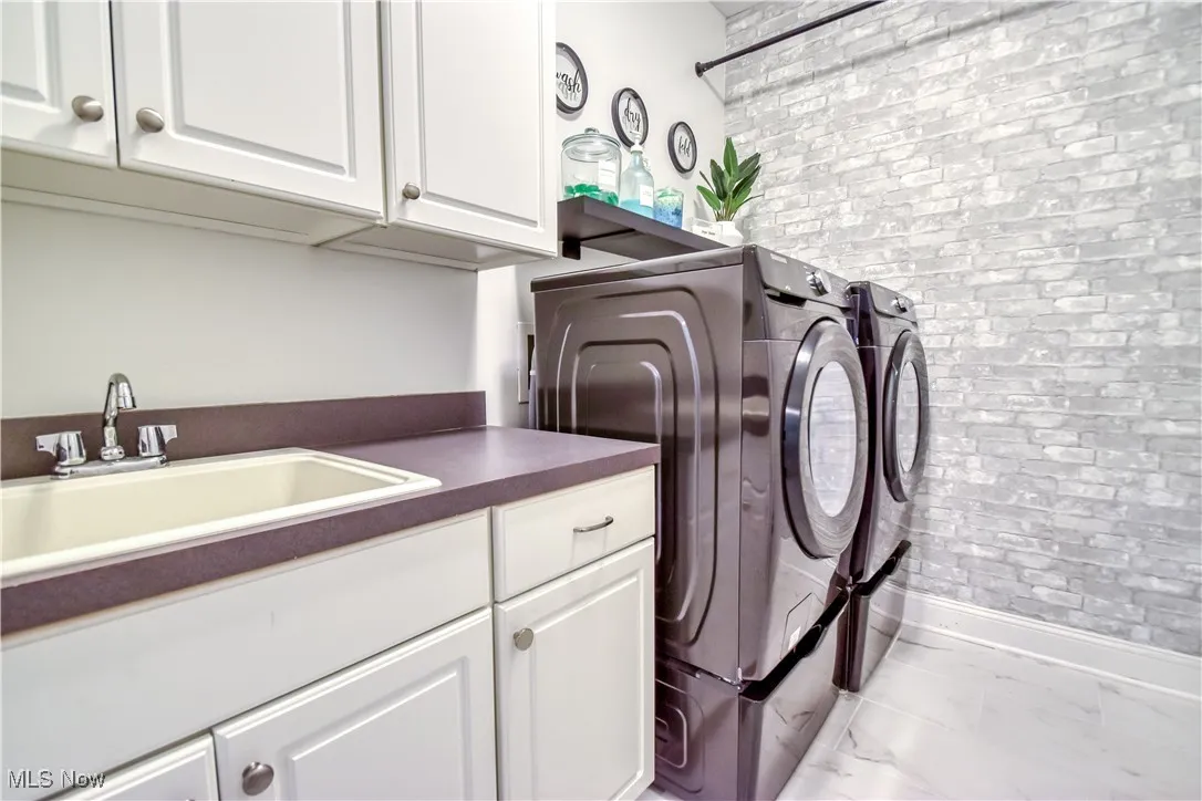 Washroom featuring washer and dryer, cabinet space, brick wall, and marble finish floors