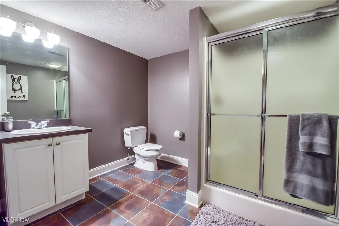 Bathroom featuring vanity, a shower with door, tile patterned floors, and a textured ceiling