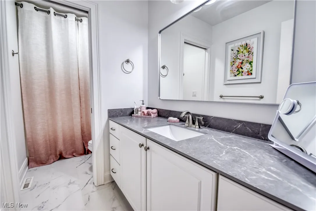 Bathroom featuring vanity, marble look tile flooring, and curtained shower