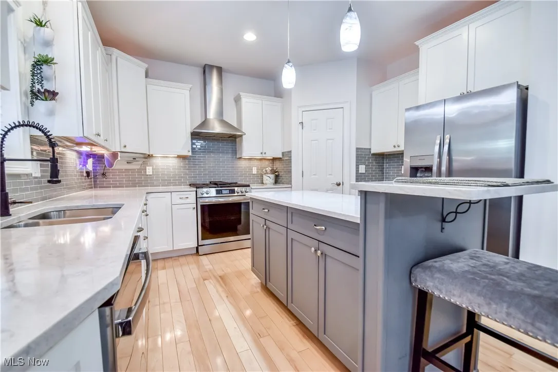 Kitchen featuring appliances with stainless steel finishes, a kitchen breakfast bar, gray cabinets, wall chimney range hood, and white cabinets