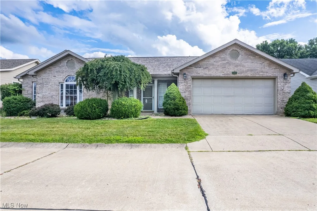 Ranch-style house featuring brick siding, an attached garage, driveway, a front lawn, and a shingled roof