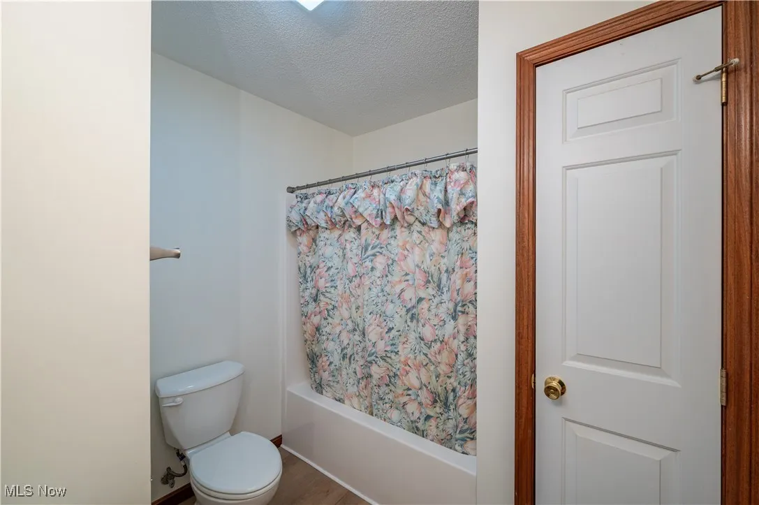 Bathroom with a textured ceiling, shower / bath combo with shower curtain, and wood finished floors