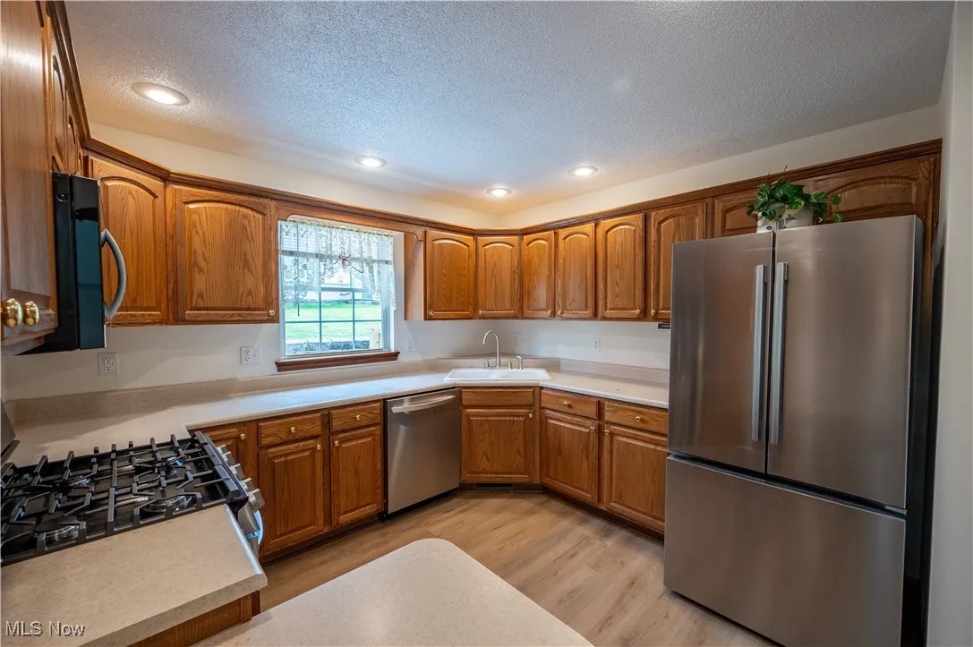 Kitchen featuring appliances with stainless steel finishes, a textured ceiling, brown cabinetry, light wood-style flooring, and light countertops
