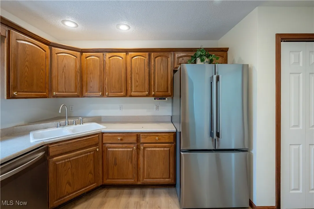 Kitchen with appliances with stainless steel finishes, brown cabinetry, light countertops, a textured ceiling, and light wood-style flooring