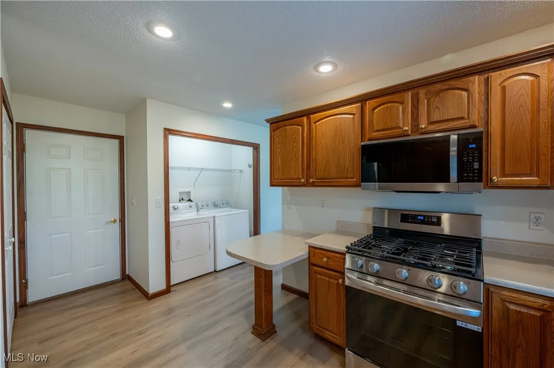 Kitchen featuring independent washer and dryer, appliances with stainless steel finishes, light countertops, light wood finished floors, and brown cabinetry