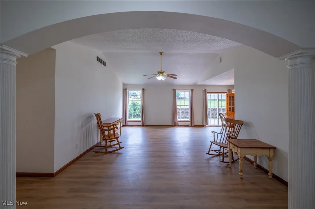 Sitting room with wood finished floors, ornate columns, a ceiling fan, vaulted ceiling, and a textured ceiling