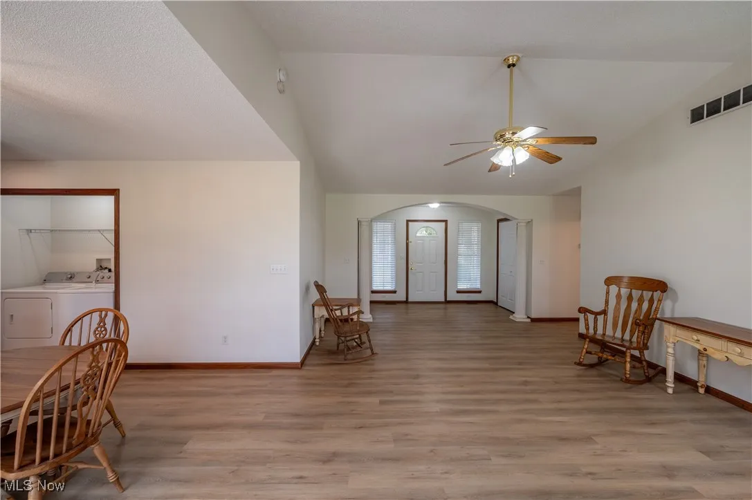 Living area with arched walkways, vaulted ceiling, a ceiling fan, light wood-style flooring, and independent washer and dryer