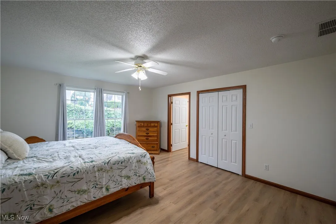 Bedroom with light wood-style flooring, a textured ceiling, a ceiling fan, and a closet