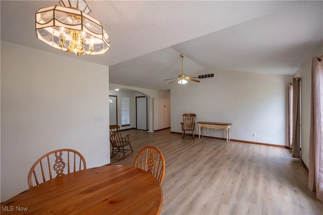 Dining room with arched walkways, ceiling fan, lofted ceiling, light wood finished floors, and a chandelier