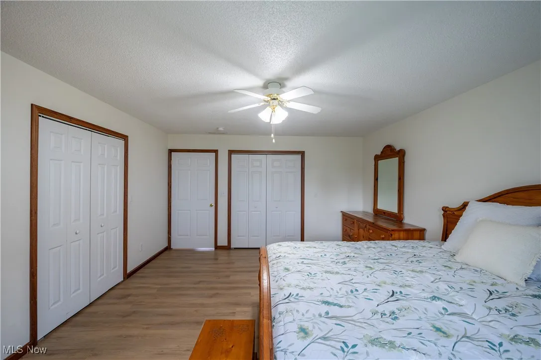 Bedroom featuring light wood-style floors, two closets, a textured ceiling, and a ceiling fan