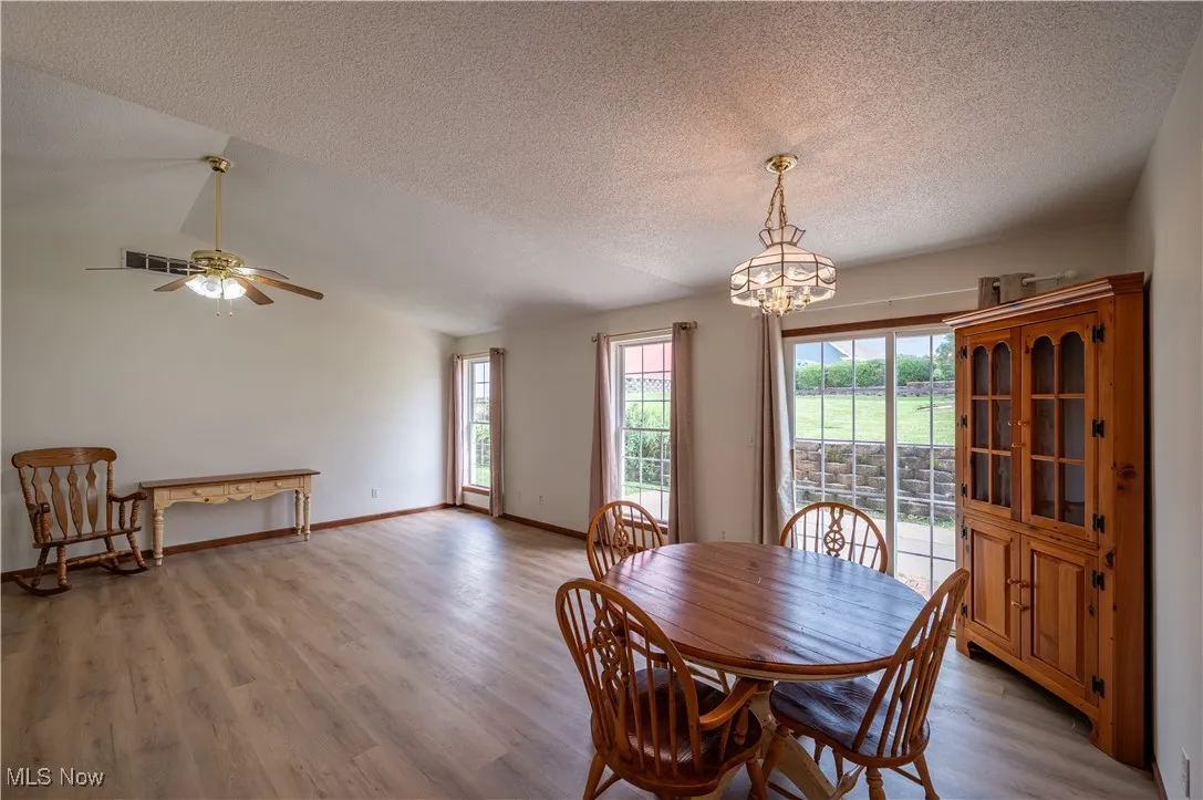 Dining room with plenty of natural light, a textured ceiling, light wood-type flooring, a chandelier, and a ceiling fan