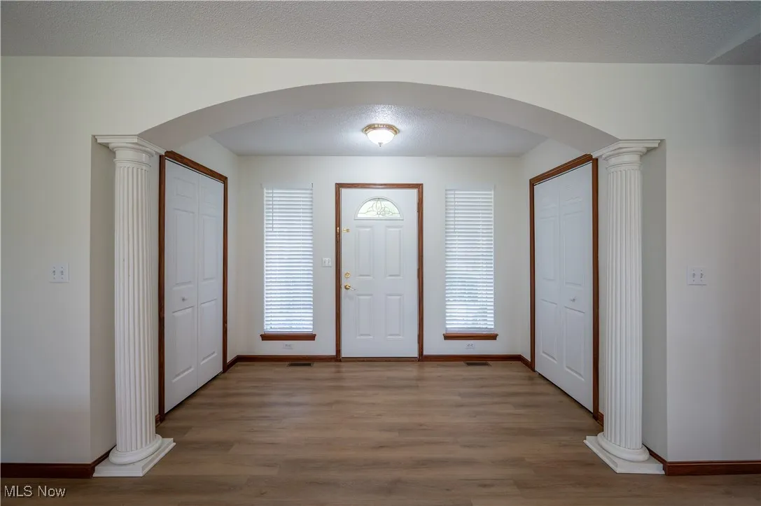 Entrance foyer featuring arched walkways, decorative columns, and wood finished floors