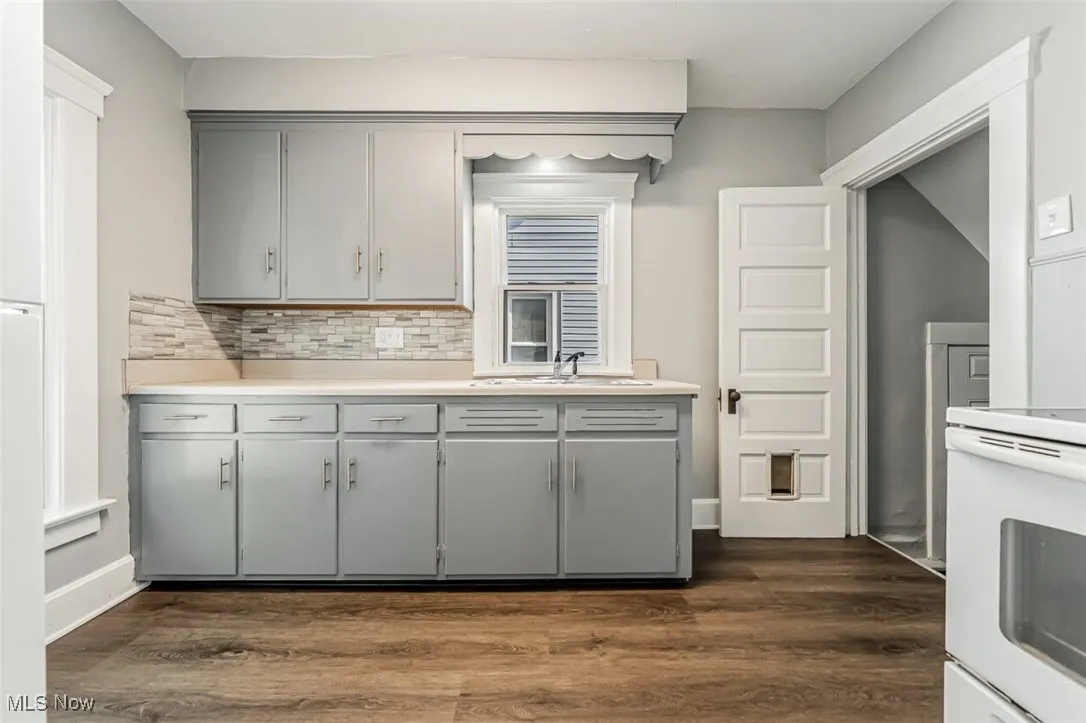 Kitchen featuring gray cabinets, white range, dark wood-type flooring, and light countertops