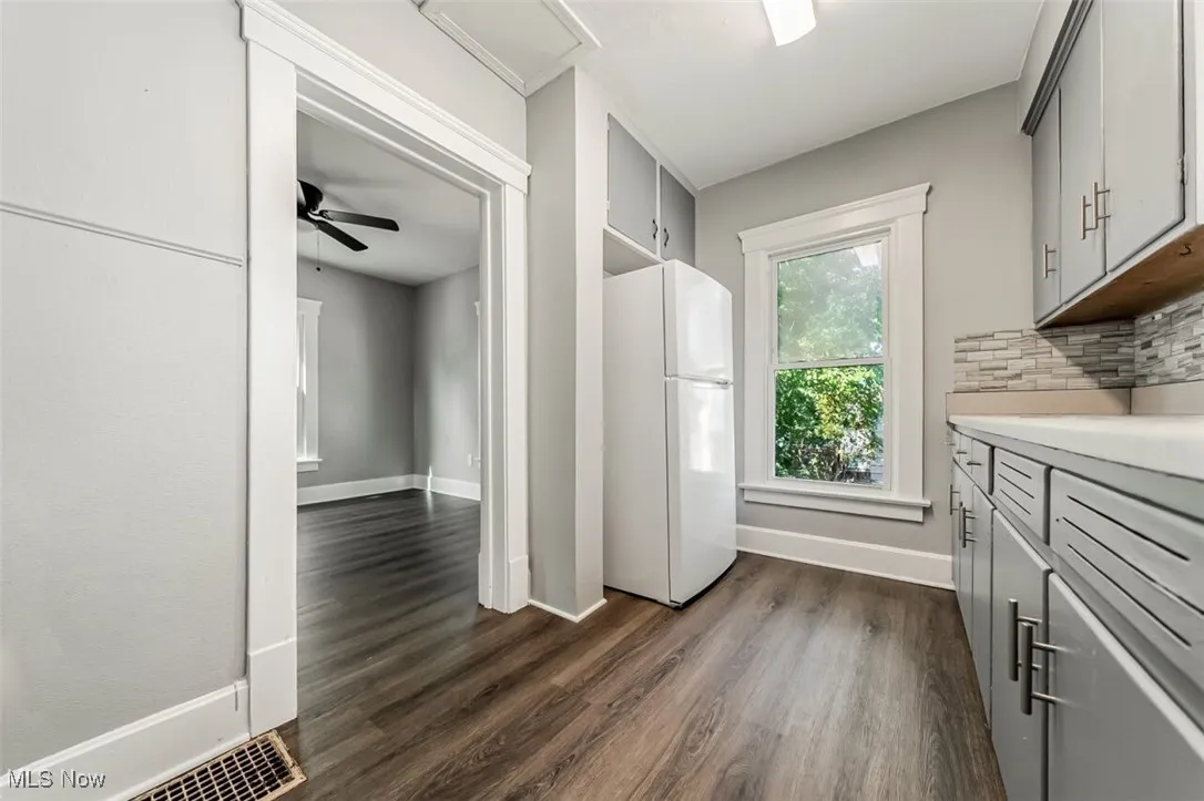 Kitchen featuring freestanding refrigerator, gray cabinets, light countertops, dark wood-style flooring, and decorative backsplash