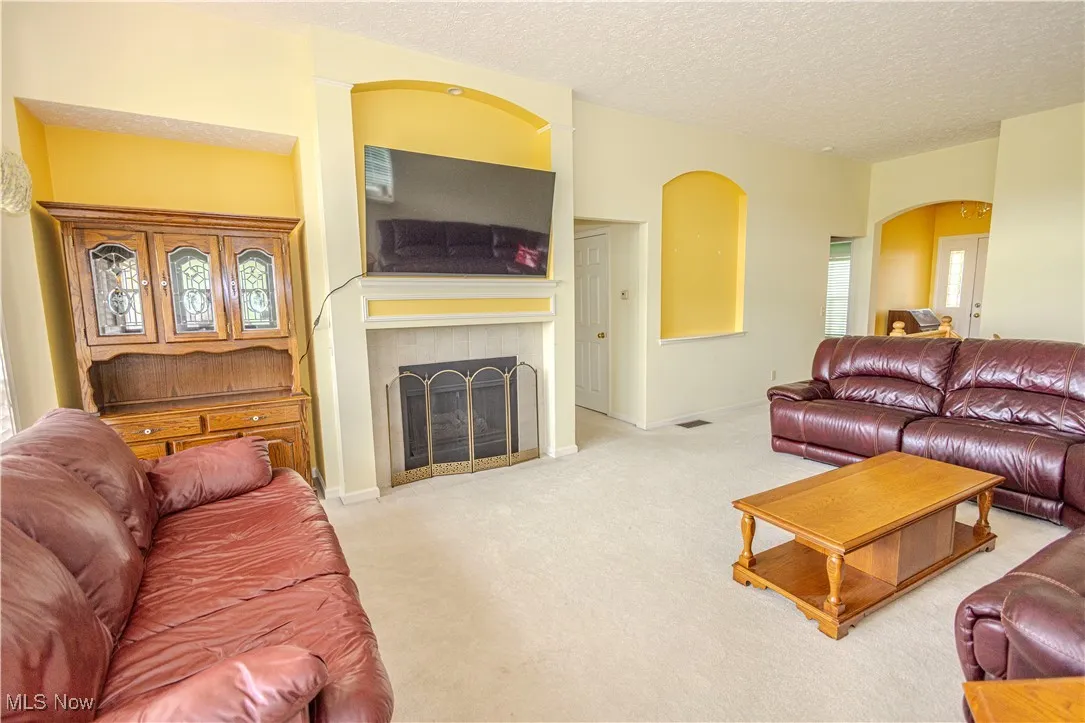 Carpeted living area featuring arched walkways, a textured ceiling, and a fireplace