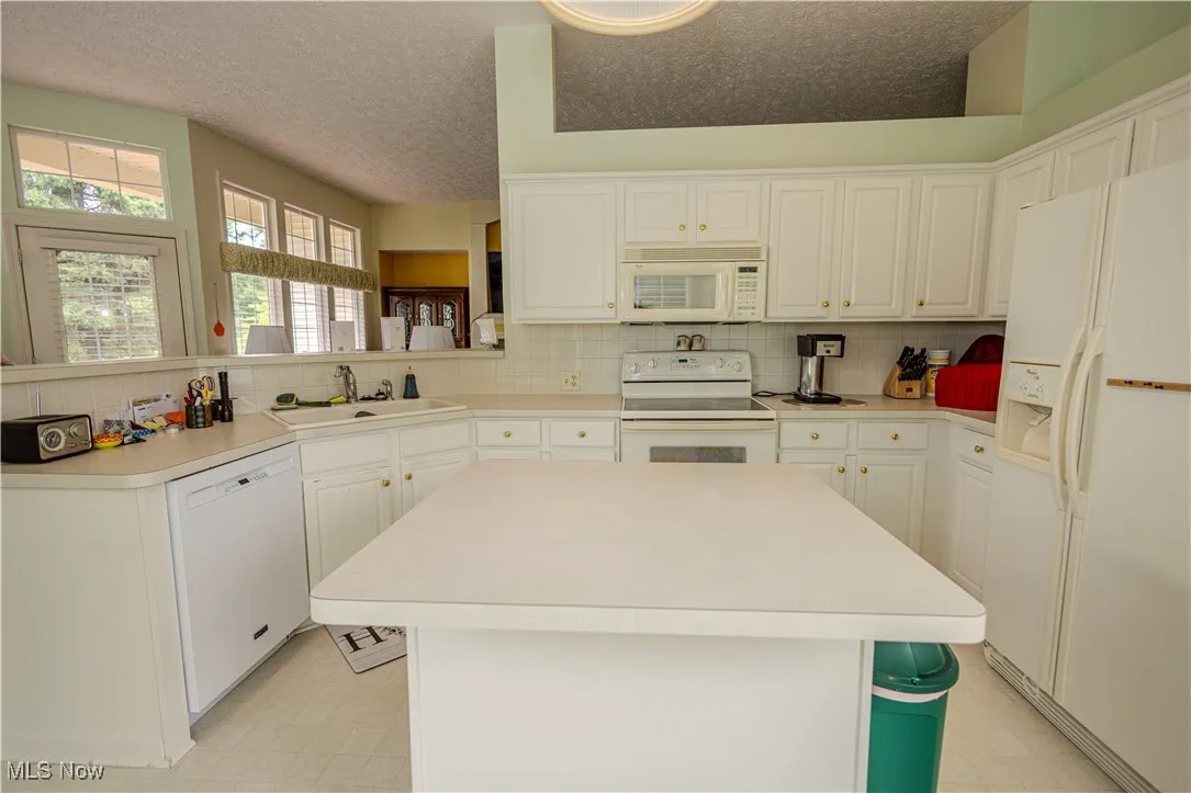 Kitchen featuring white appliances, decorative backsplash, a textured ceiling, white cabinets, and a center island