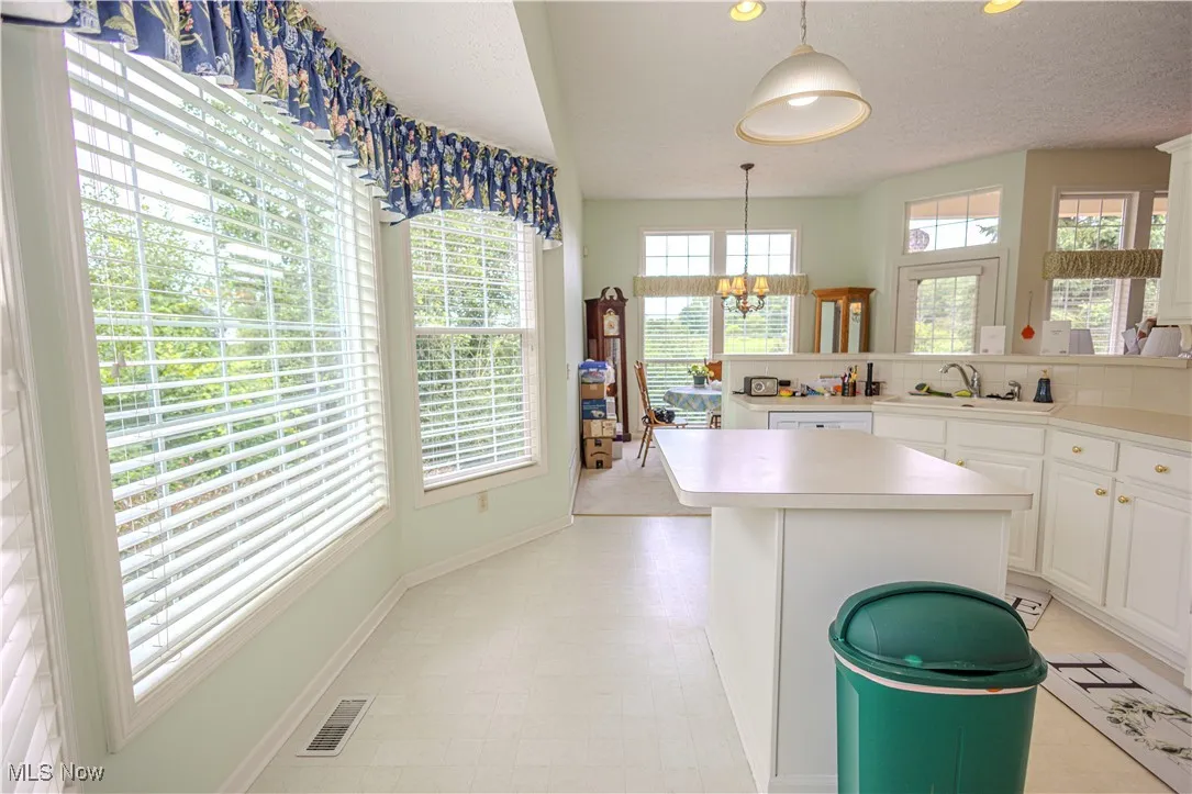 Kitchen with a chandelier, a kitchen island, light countertops, hanging light fixtures, and a textured ceiling