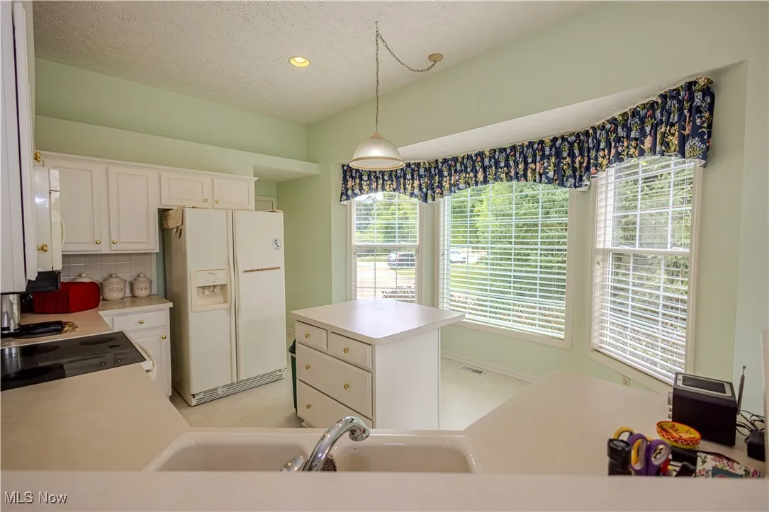 Kitchen with white fridge with ice dispenser, light countertops, a kitchen island, a textured ceiling, and white cabinets