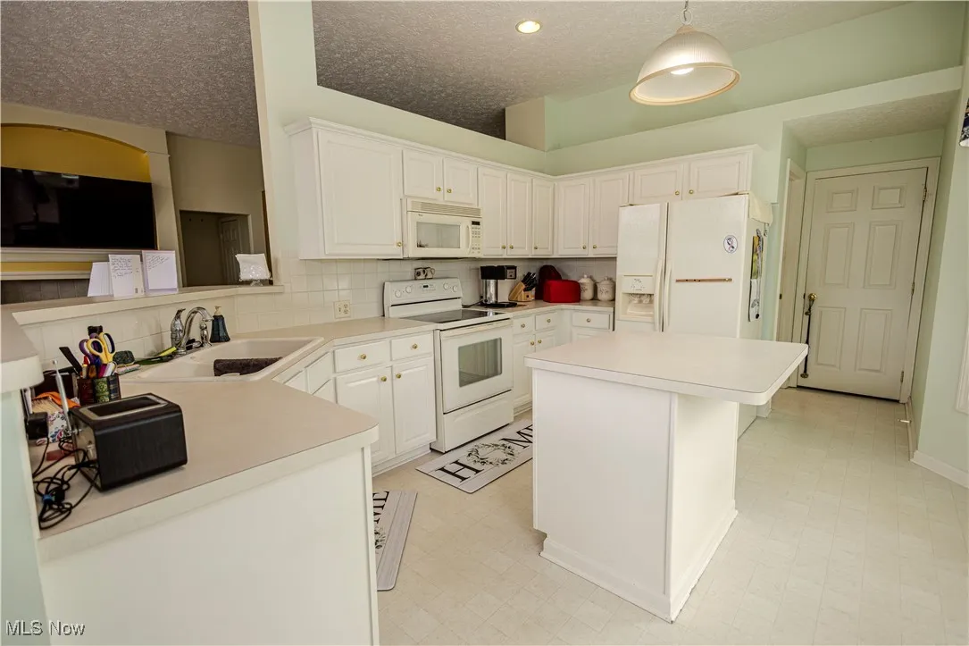 Kitchen with white appliances, a textured ceiling, light countertops, a center island, and white cabinets
