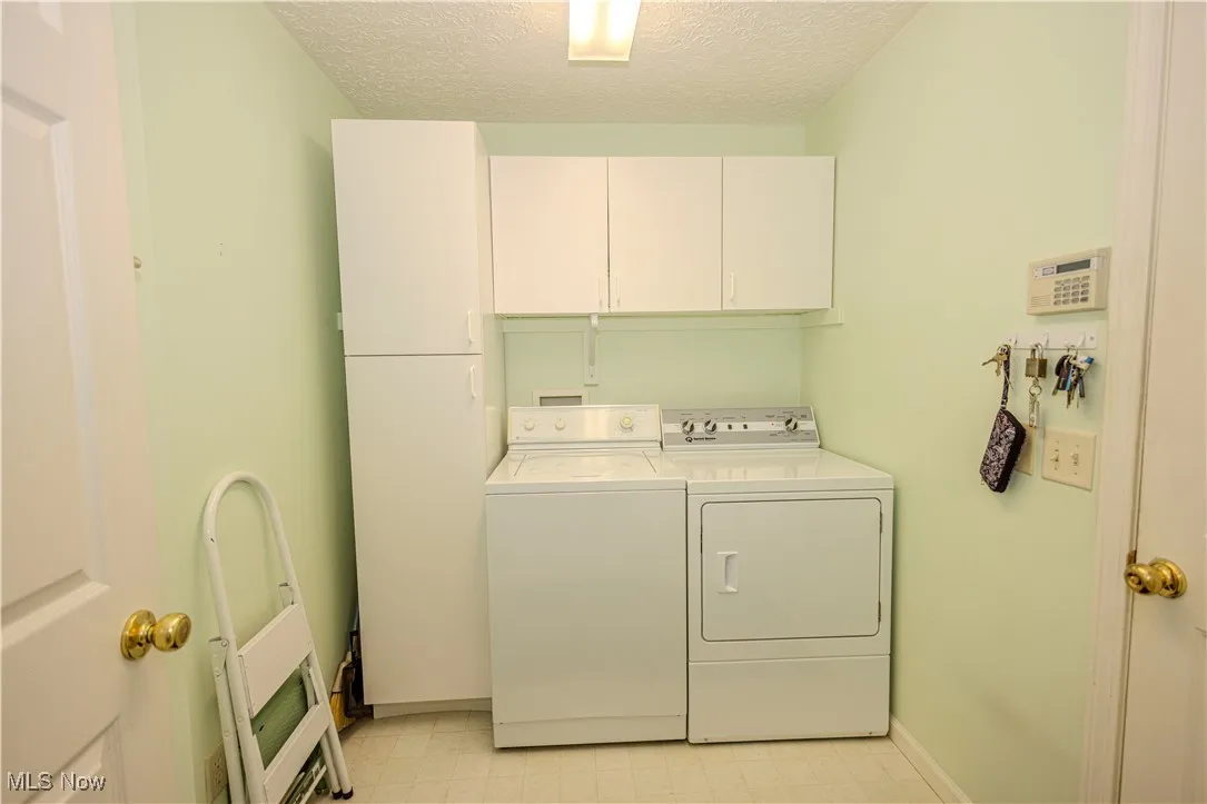 Washroom with cabinet space, washer and clothes dryer, a textured ceiling, and light flooring