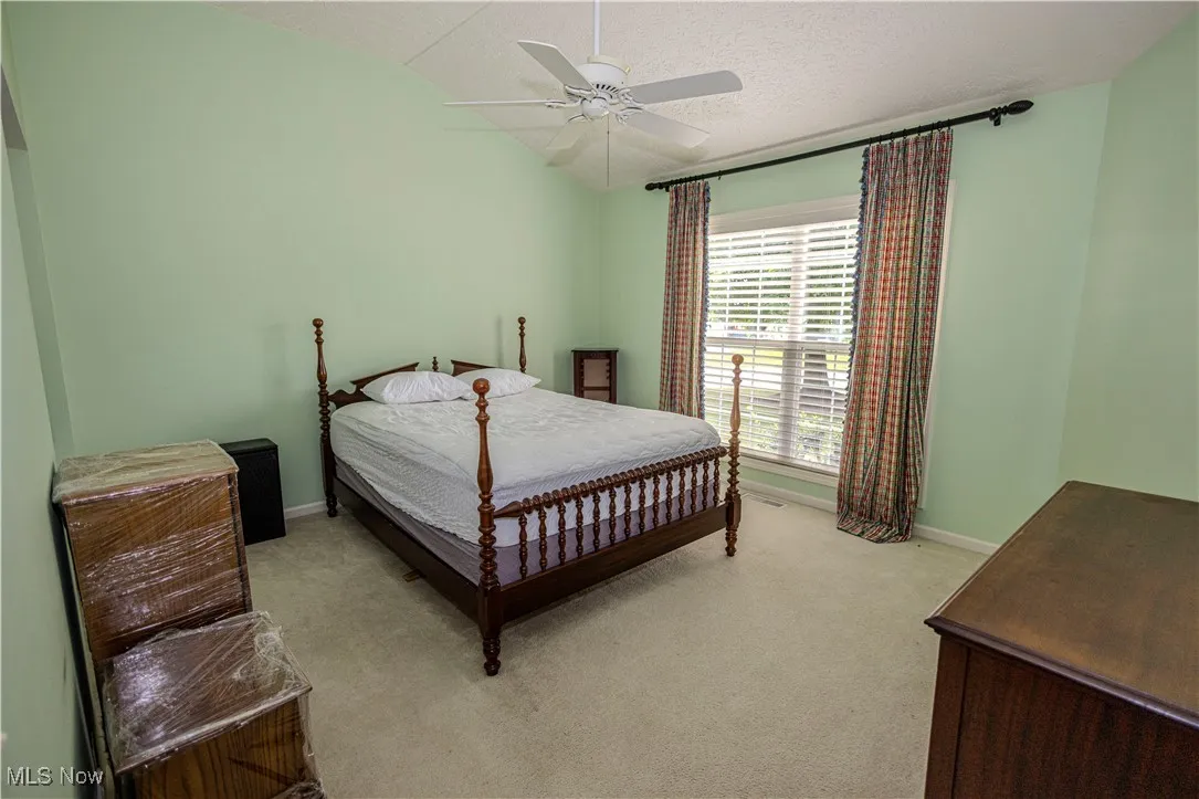 Bedroom with light carpet, lofted ceiling, ceiling fan, and a textured ceiling