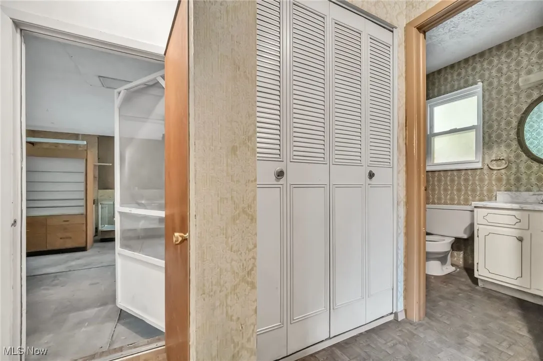Bathroom featuring wallpapered walls, a closet, vanity, and wood finished floors