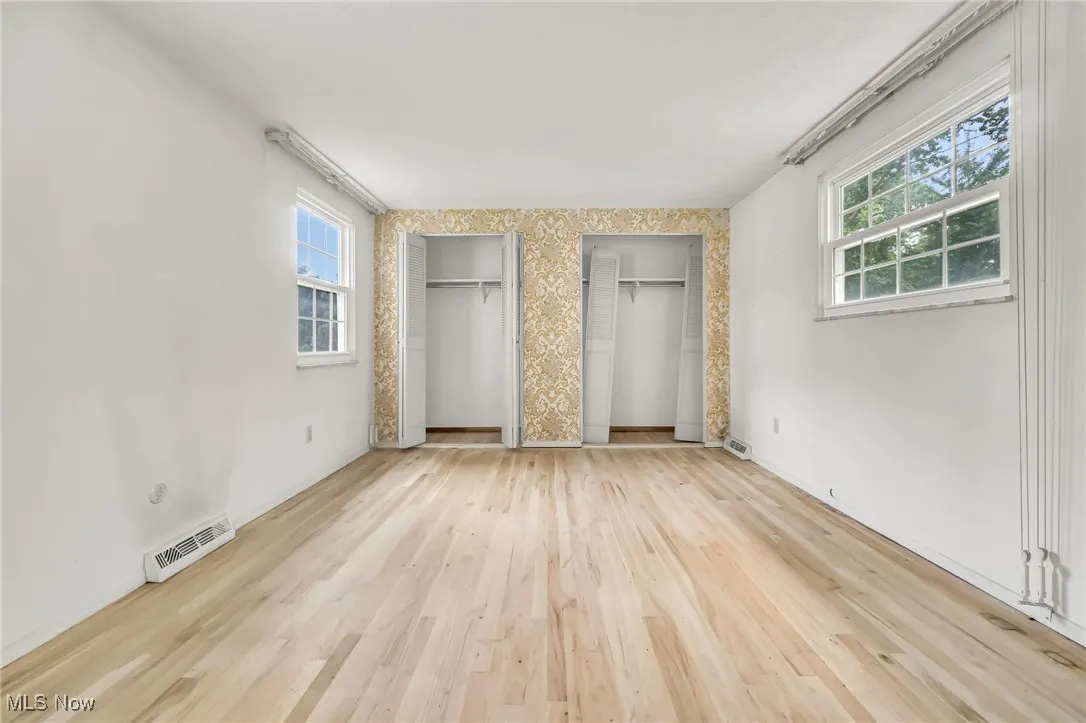 Unfurnished bedroom with two closets, wood finished floors, and wallpapered walls
