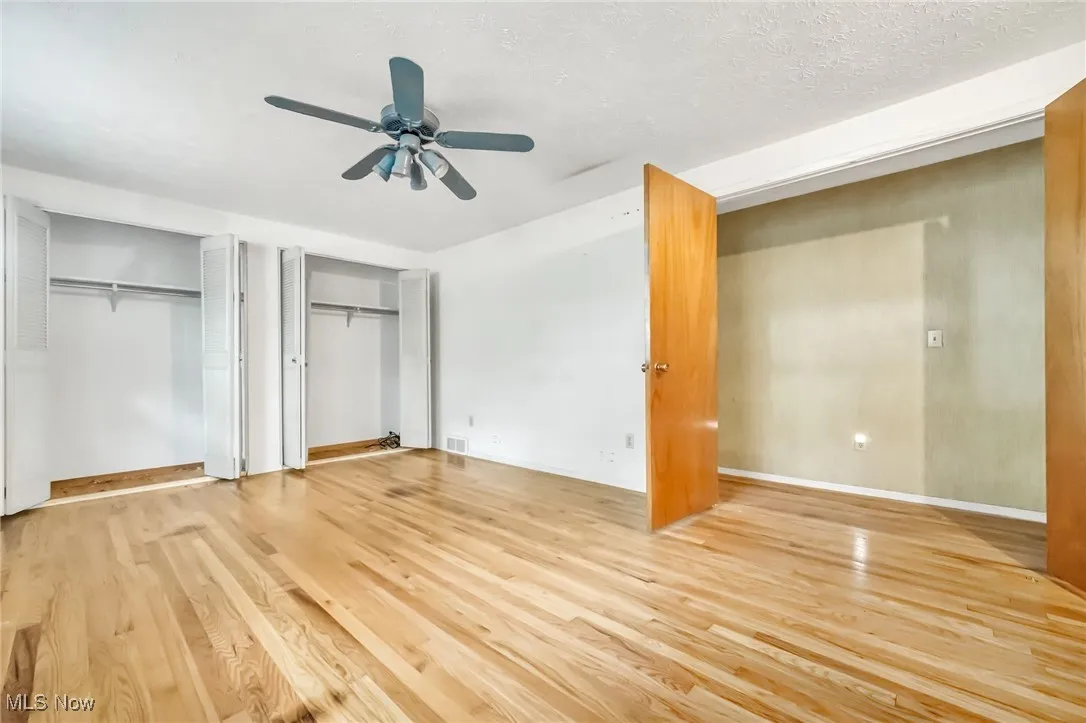 Unfurnished bedroom featuring multiple closets, wood finished floors, and a ceiling fan