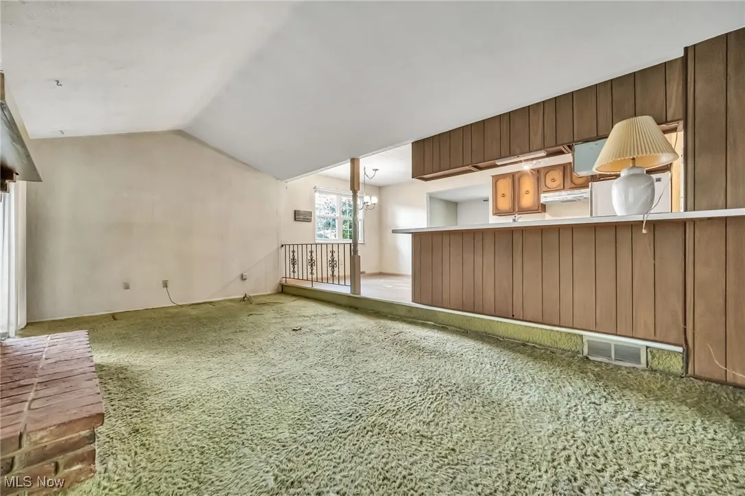 Unfurnished living room with carpet flooring, lofted ceiling, and a chandelier