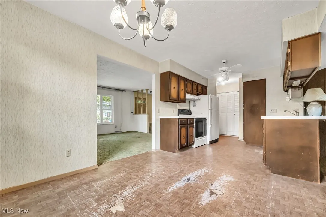 Kitchen featuring light countertops, stove, a chandelier, a ceiling fan, and wallpapered walls