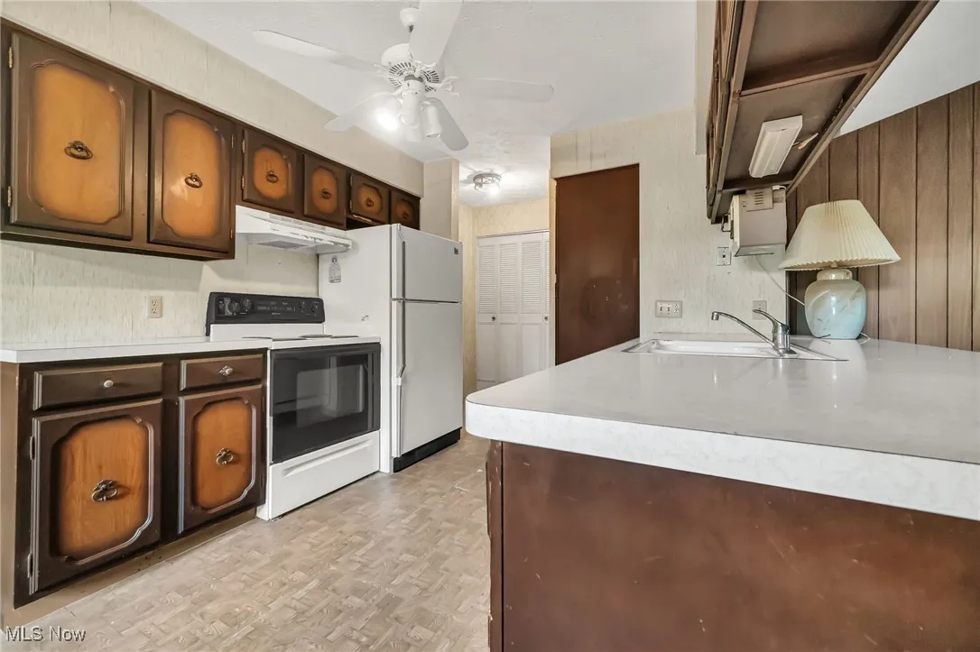 Kitchen with white electric range, light countertops, under cabinet range hood, and a ceiling fan