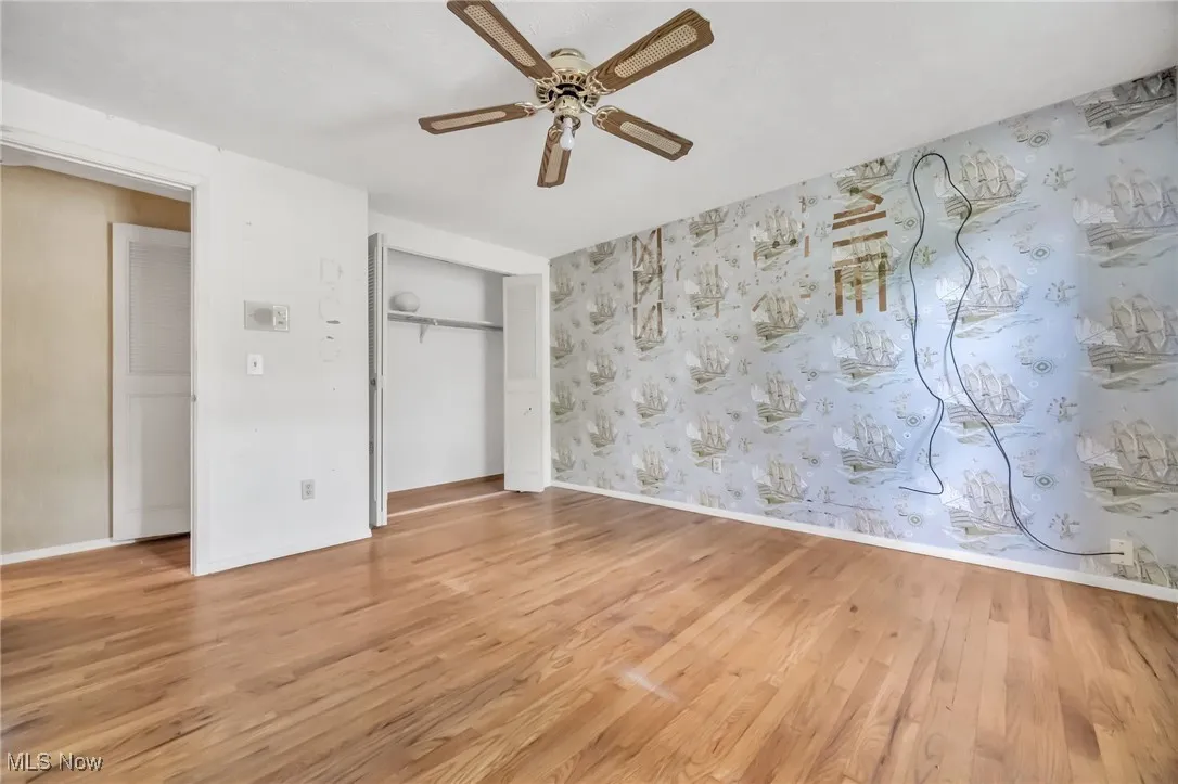 Unfurnished bedroom with light wood-style flooring, a closet, ceiling fan, and wallpapered walls