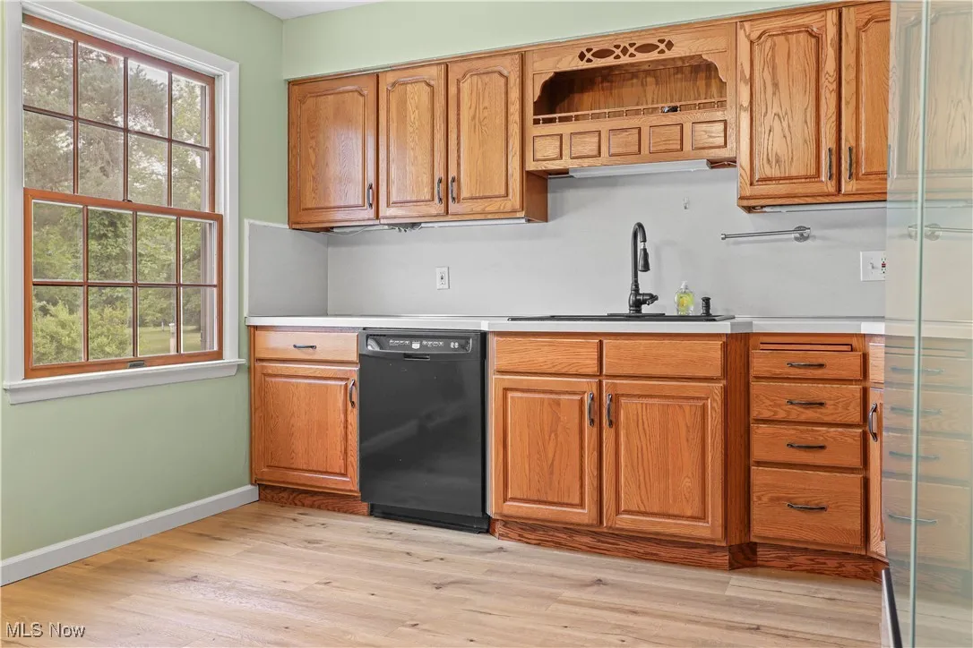 Kitchen with light countertops, black dishwasher, light wood-type flooring, and brown cabinetry