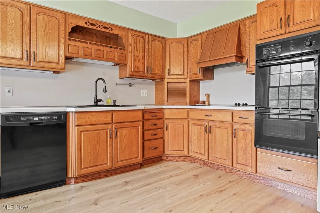 Kitchen with black appliances, custom exhaust hood, light wood-style floors, and light countertops
