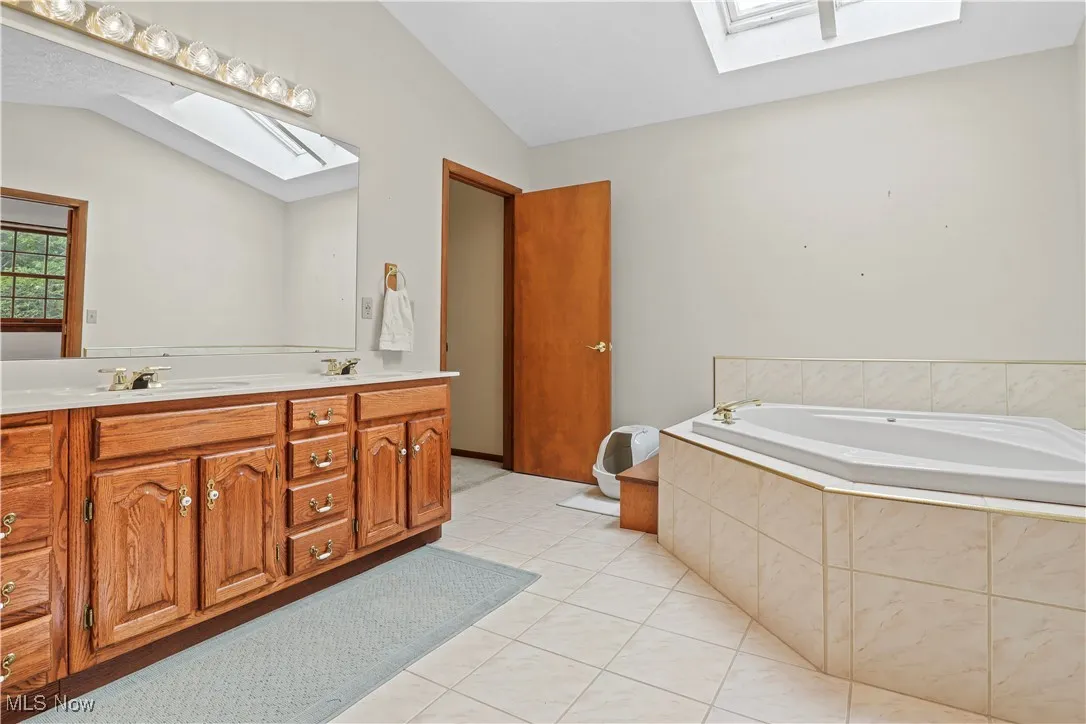 Full bath featuring a skylight, lofted ceiling, double vanity, tile patterned floors, and a bath