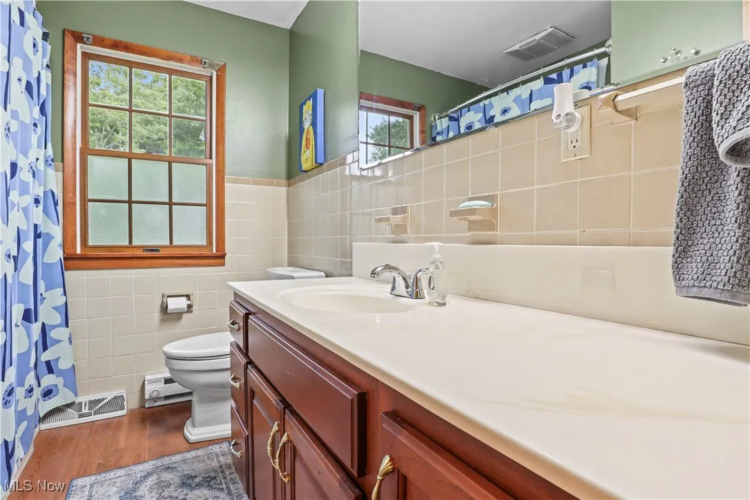 Main Floor Bathroom featuring tile walls, vanity, wood finished floors, a baseboard radiator, and a shower with curtain