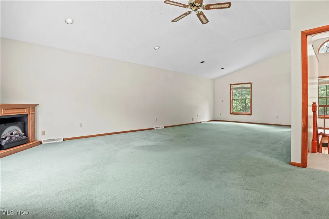 Unfurnished living room with carpet flooring, a ceiling fan, vaulted ceiling, a fireplace with raised hearth, and recessed lighting