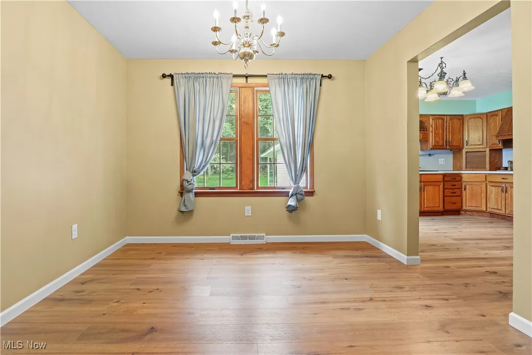 Unfurnished dining area off the kitchen with a chandelier and light wood finished floors