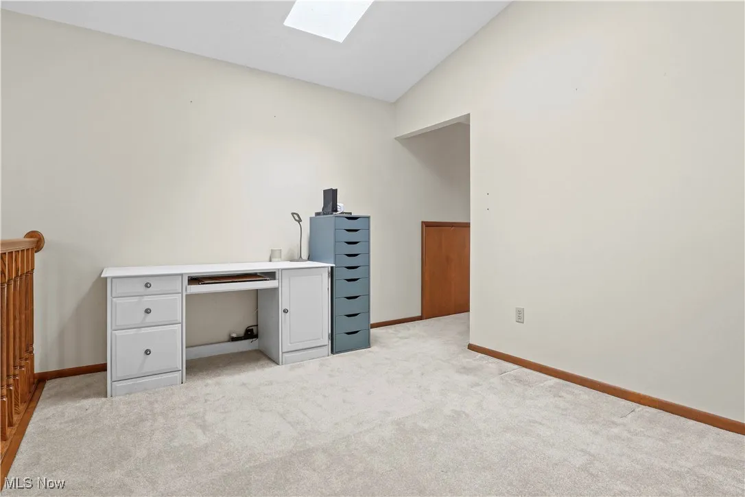 Unfurnished office with light carpet, a skylight, and high vaulted ceiling overlooking the foyer and staircase.