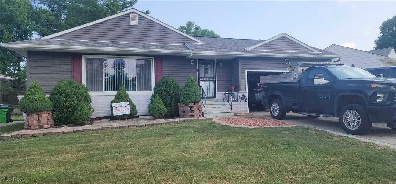 Ranch-style home featuring an attached garage, a front yard, roof with shingles, driveway, and brick siding