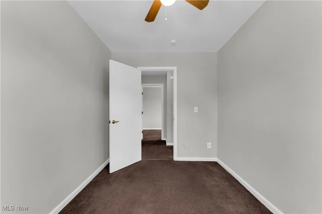 Unfurnished room with a ceiling fan and dark colored carpet