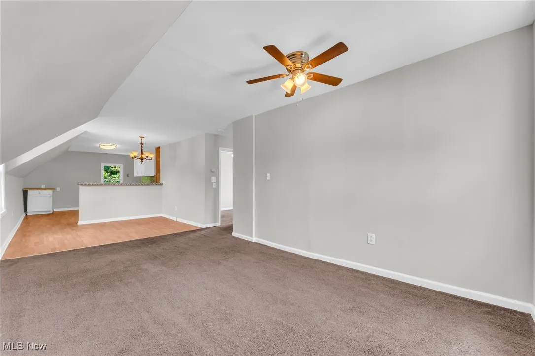 Unfurnished living room featuring carpet, a ceiling fan, a chandelier, and vaulted ceiling