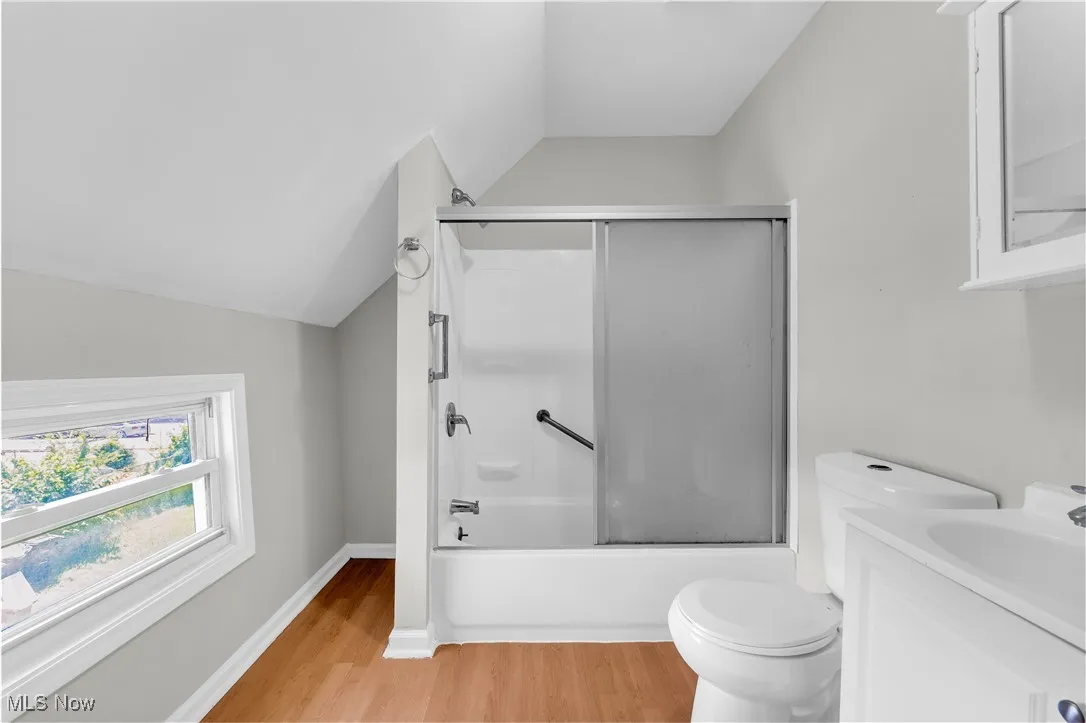 Full bath featuring lofted ceiling, wood finished floors, shower / bath combination with glass door, and vanity