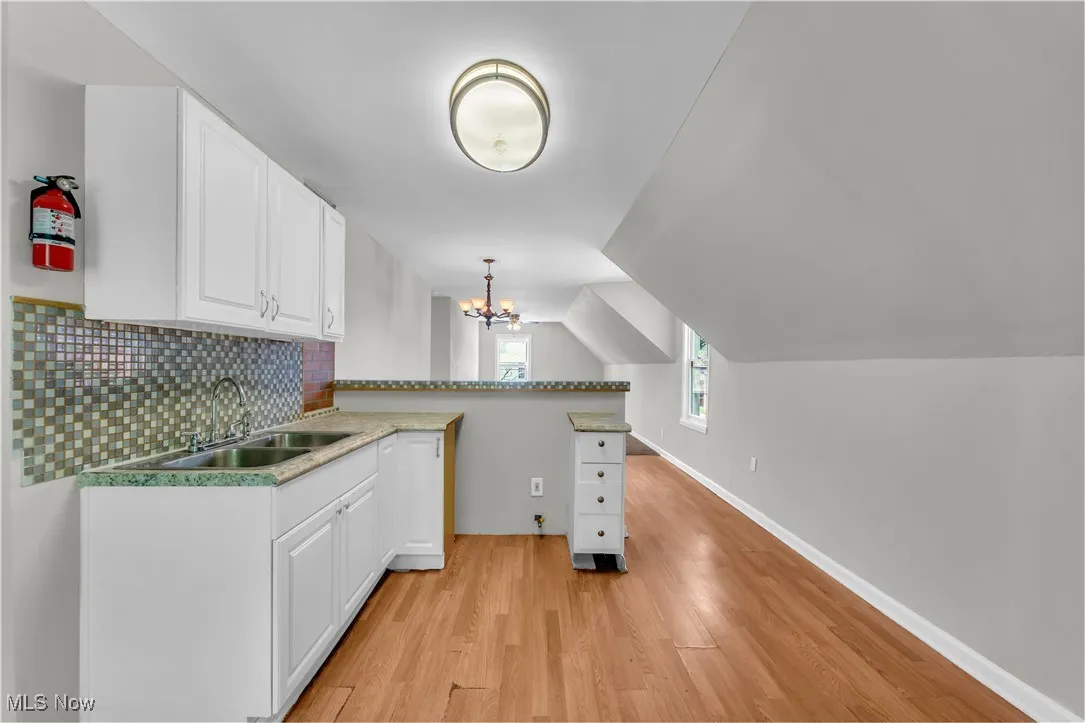 Kitchen with light wood-type flooring, a peninsula, white cabinetry, backsplash, and a chandelier