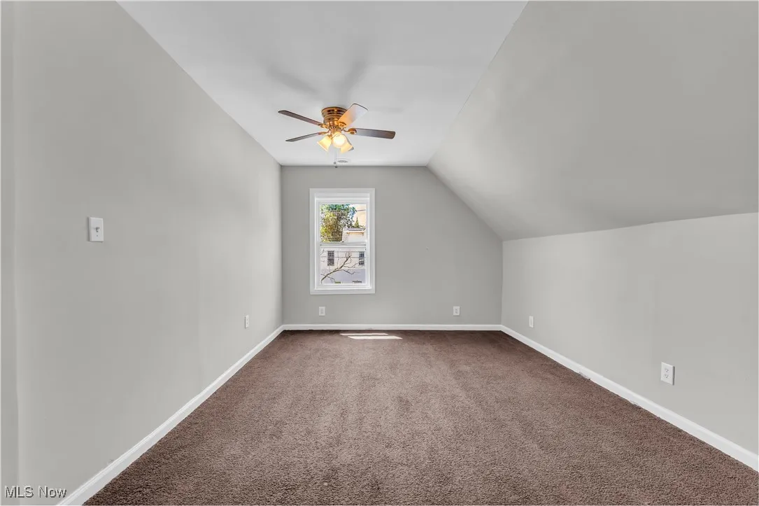 Additional living space with a ceiling fan, dark colored carpet, and vaulted ceiling
