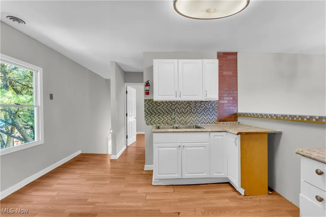 Kitchen featuring white cabinetry, tasteful backsplash, light wood-style flooring, and light stone counters