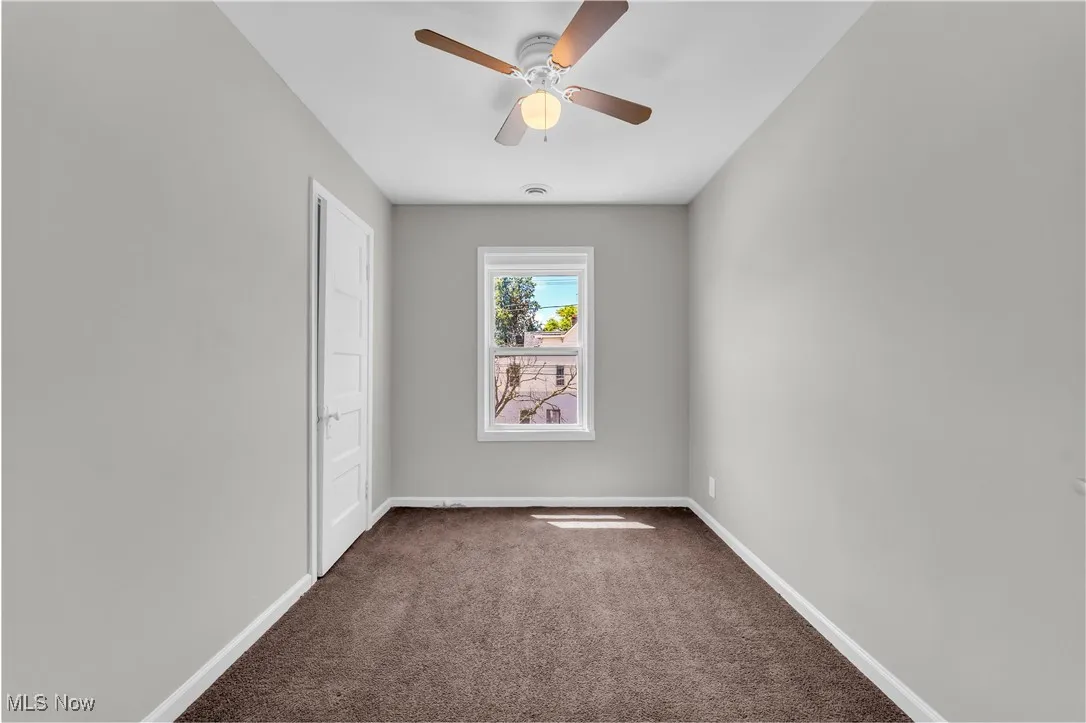 Unfurnished room featuring dark colored carpet and a ceiling fan