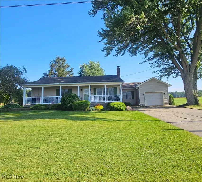 Single story home featuring covered porch, a chimney, driveway, and an attached garage