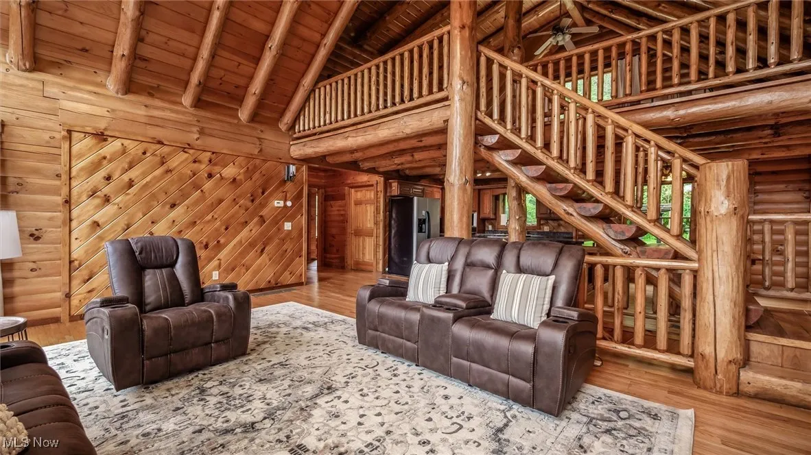 Living area with log walls, a wood ceiling with exposed beams, high vaulted ceiling, wood finished floors, and a ceiling fan