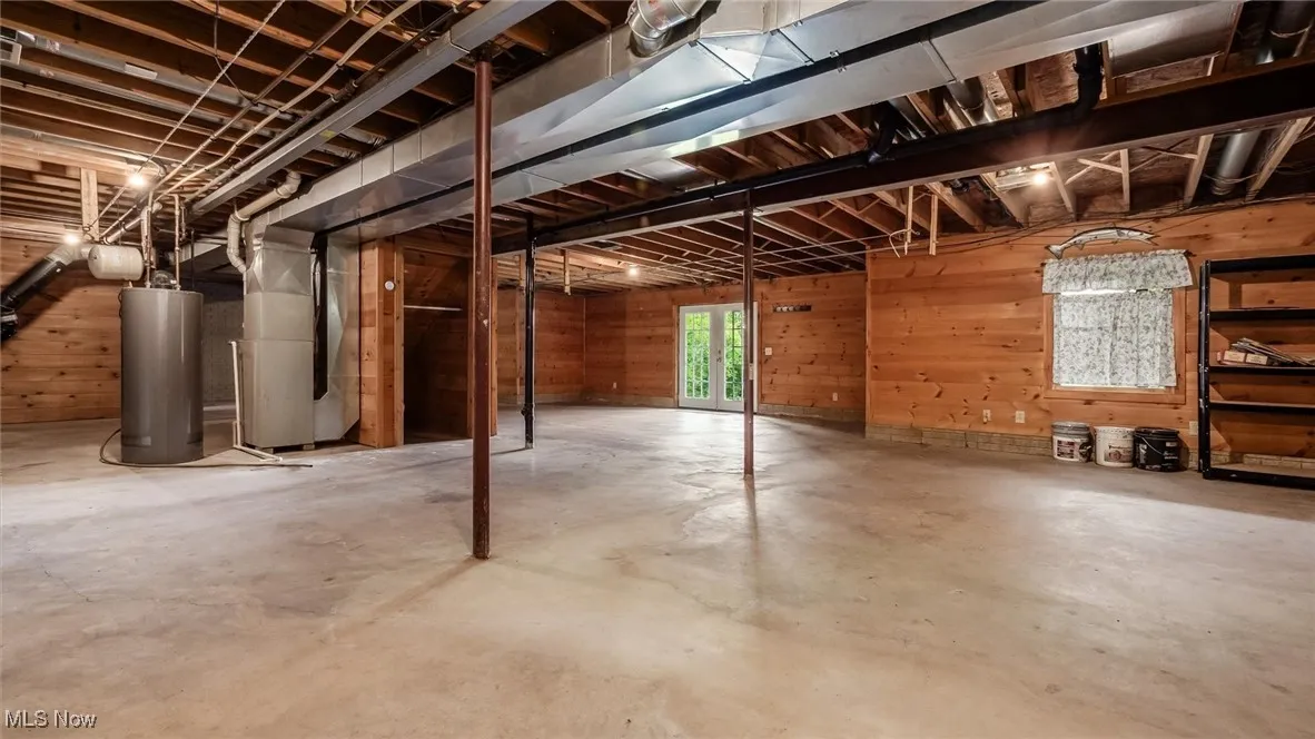 Basement with wood walls, water heater, and heating unit
